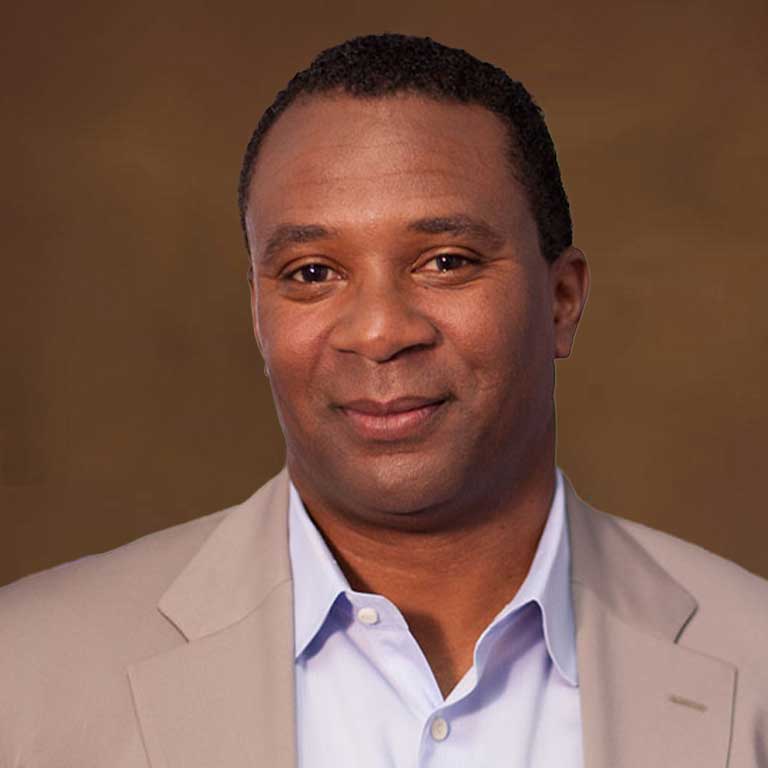 Headshot of Isaac Vaughn wearing a tan suit and light blue shirt